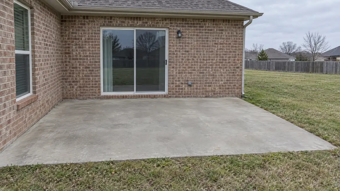 Before: Open Patio | Music City Deck & Fence Before: A plain open concrete patio against the back wall of a brick home with a sliding door