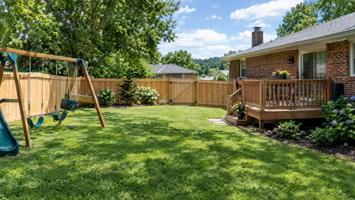 A suburban backyard with a new six-foot dog-eared cedar privacy fence, a walk gate, a swing set and a small deck