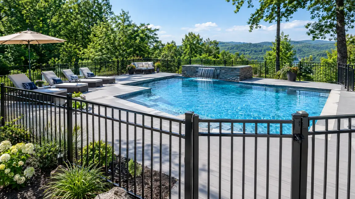 Composite Pool Deck and Safety Fence | Music City Deck & Fence A swimming pool surrounded by a light gray composite deck with a black aluminum safety fence, a self-closing gate and lounge chairs