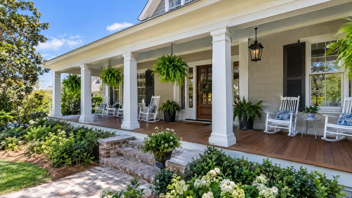 A Southern craftsman front porch with white columns, a wide wood floor, rocking chairs and hanging ferns